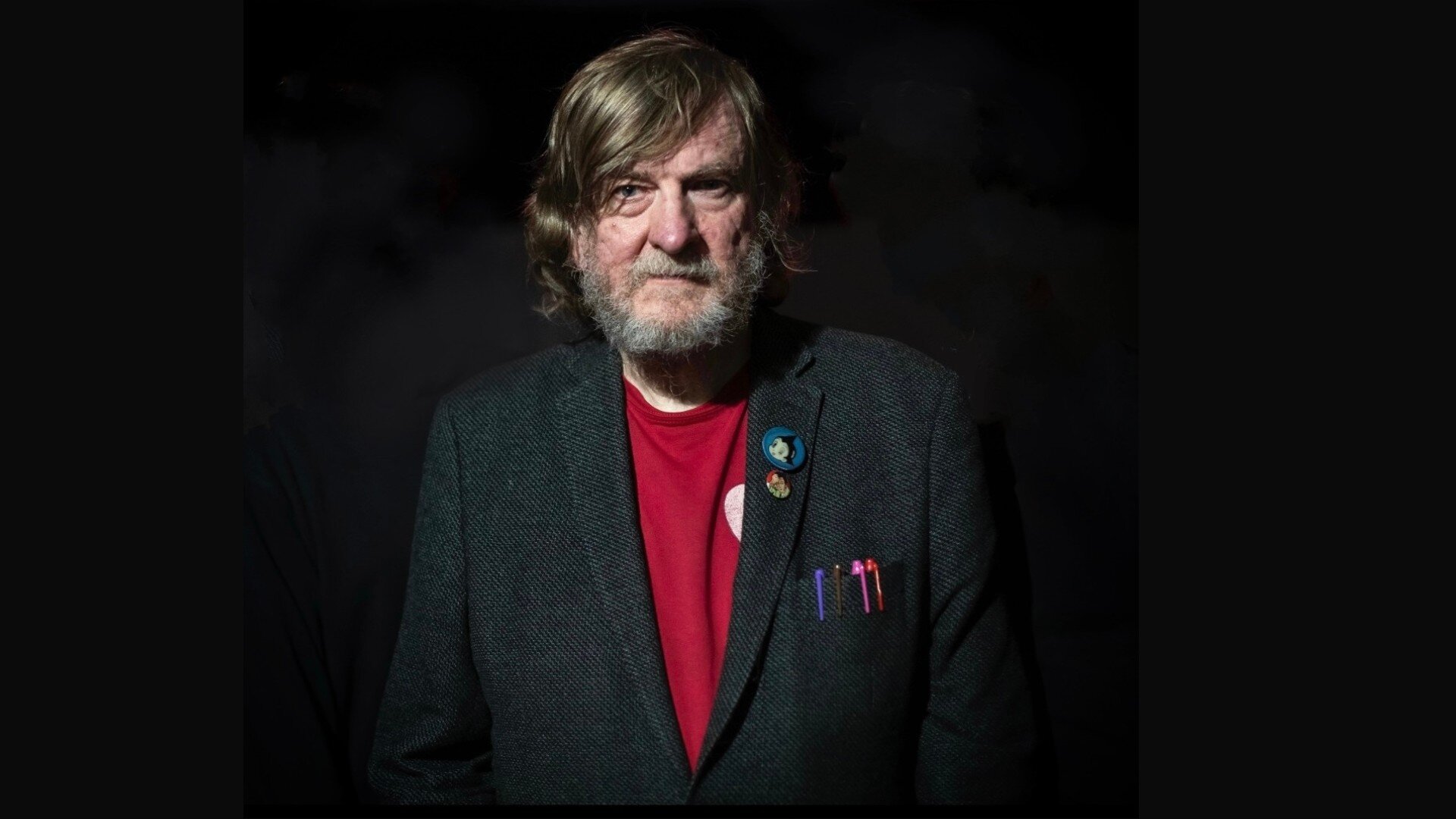 Portrait of an older man with badges, dark background, celebrating gaming and music event.